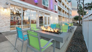 An outdoor seating area with fire pits and chairs, a stone facade building, and a balcony with railings.