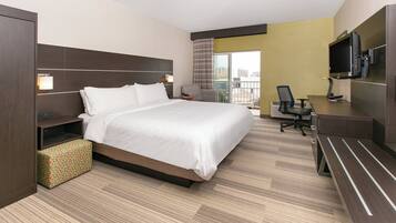 A hotel room with a bed, desk, chair, television, and a view of the city.