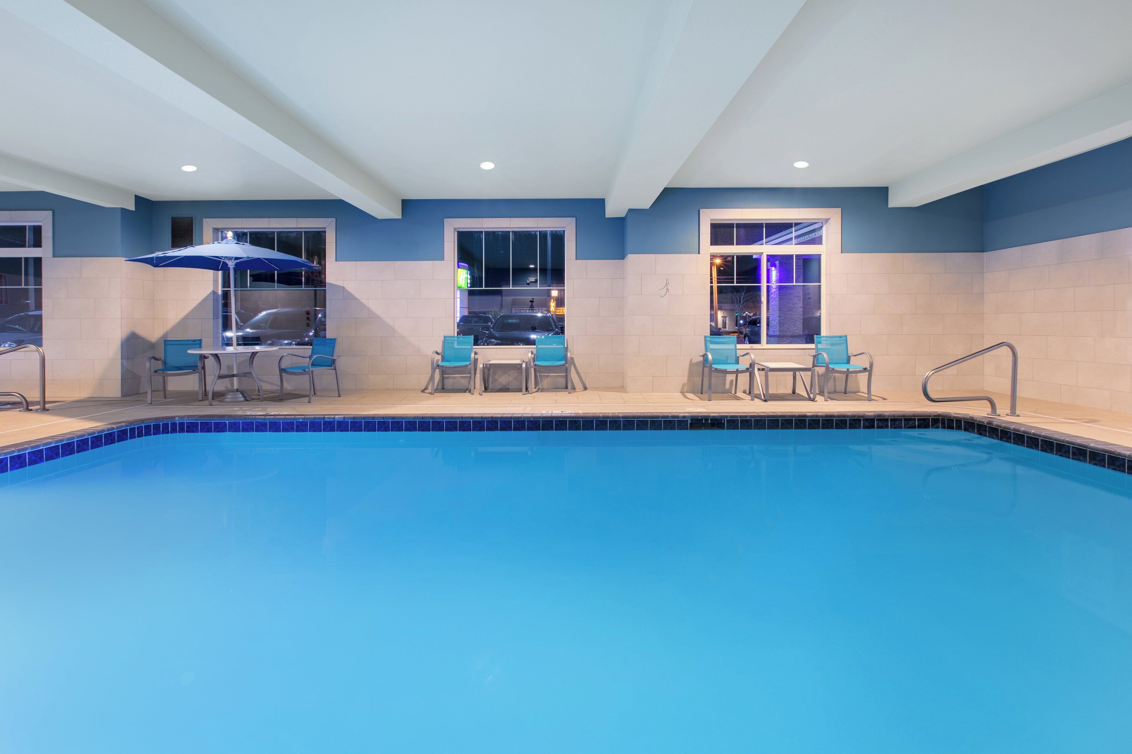 A swimming pool with blue tiles, surrounded by chairs and tables, and a ceiling with recessed lighting.