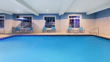 A swimming pool with blue tiles, surrounded by chairs and tables, and a ceiling with recessed lighting.
