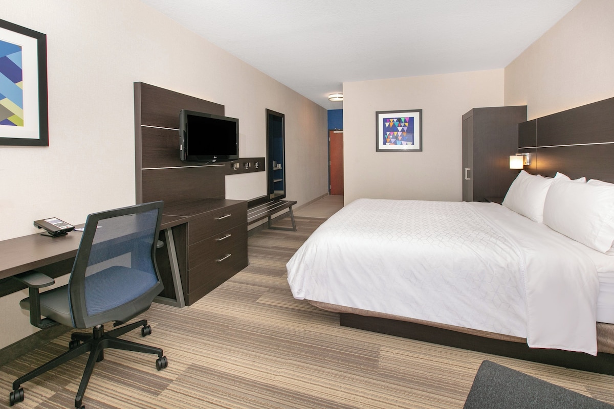 Une chambre d’hôtel équipée d’un lit, d’un bureau, d’une chaise, d’une télévision et d’œuvres d’art.