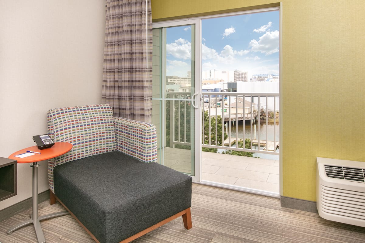 A small, modern room with a grey sofa, a small table with a telephone, and a view of a cityscape through a sliding glass door.