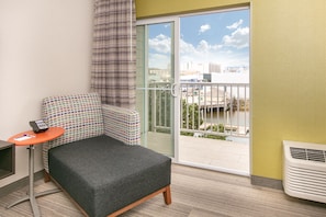 Une petite pièce moderne, avec un canapé gris, une petite table sur laquelle se trouve un téléphone, et une vue sur le paysage urbain, visible à travers une porte-fenêtre coulissante.