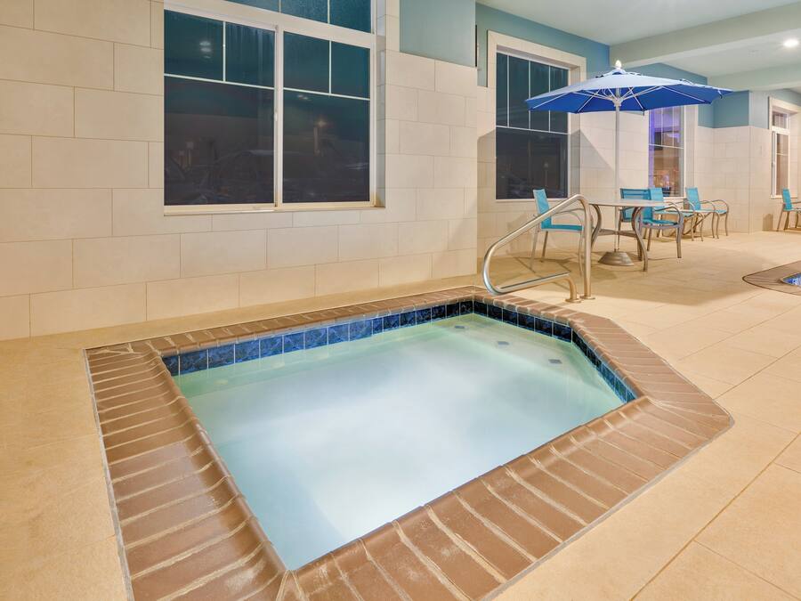 A swimming pool with a tiled edge, a chair, and a table with an umbrella.