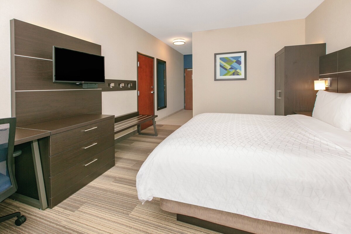 A hotel room with a bed, a desk with drawers, a television, and a door.