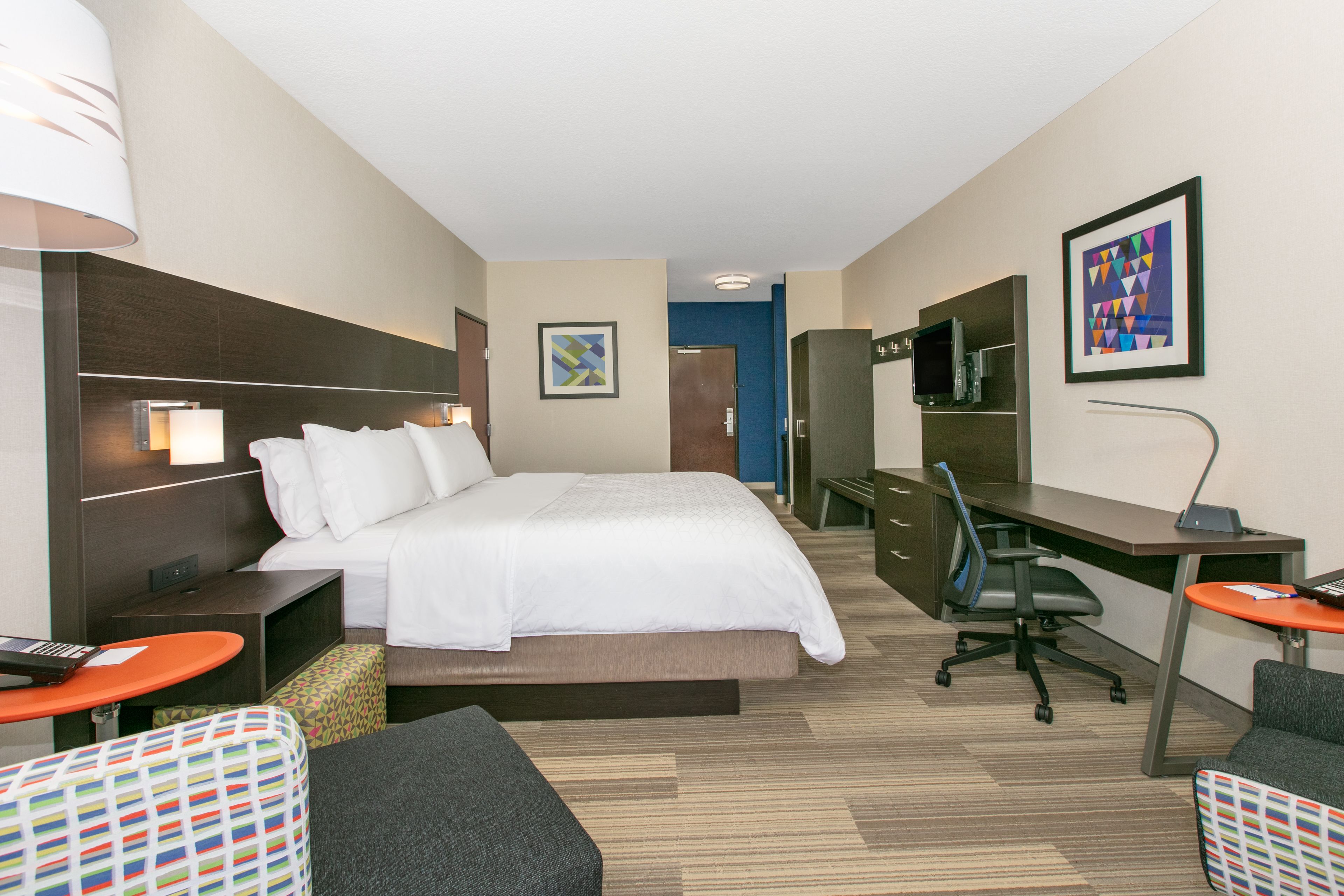 A hotel room with a bed, desk, chair, and a TV.