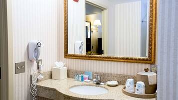 Une salle de bain d’hôtel avec un comptoir en granit, un lavabo, un miroir avec un cadre doré, un sèche-cheveux et des articles de toilette.