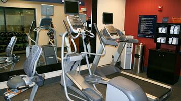 Une salle de sport équipée de tapis de course, de vélos elliptiques et d’haltères.