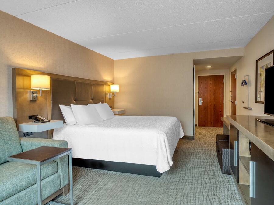 A hotel room with a bed, a desk, a chair, a TV, and a lamp.