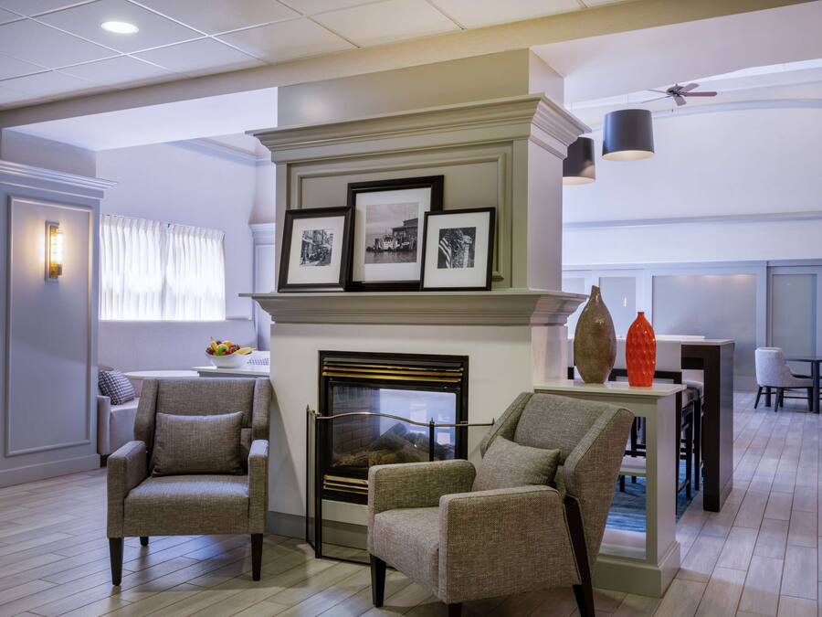 A modern living room with a fireplace, two armchairs, a dining area, and a ceiling fan.