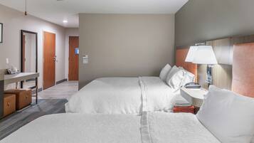 A hotel room with two beds, a desk, a chair, a lamp, and a mirror.