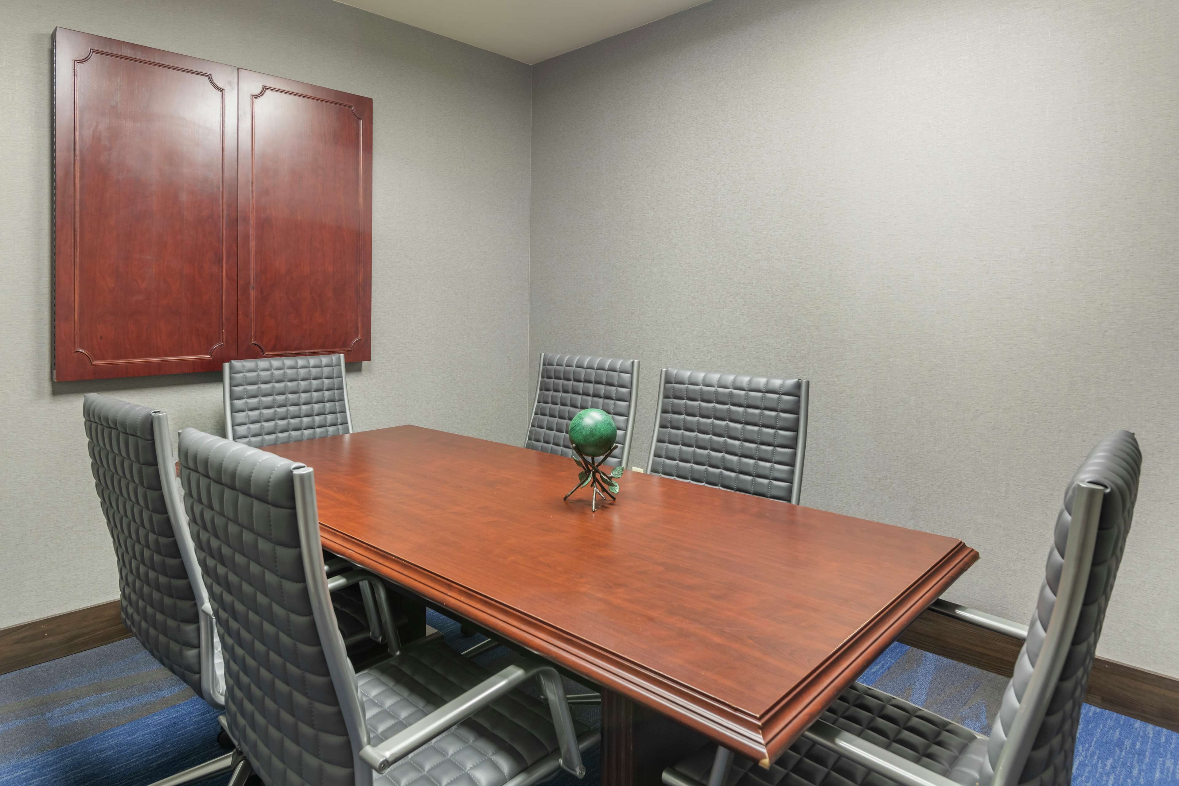 A conference room with a wooden table, six upholstered chairs, and a large wooden cabinet.