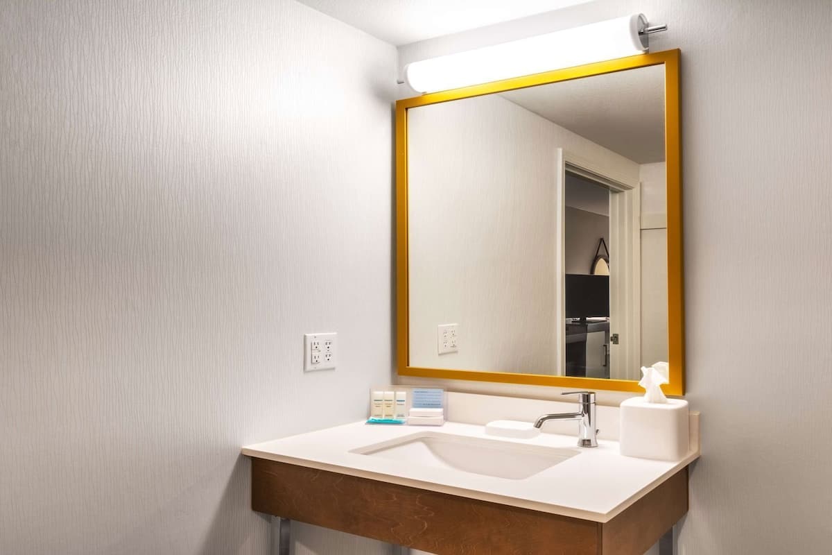 A bathroom with a white sink, a mirror with a gold frame, and a towel dispenser.