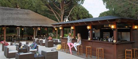 An outdoor seating area with wicker furniture and a bar with a thatched roof.