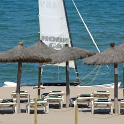 Relax by the beach with a shaded lounge area and nearby sailboat.