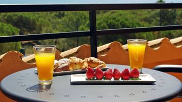 A table with breakfast items including croissants, strawberries, and glasses of orange juice, set against a scenic view.