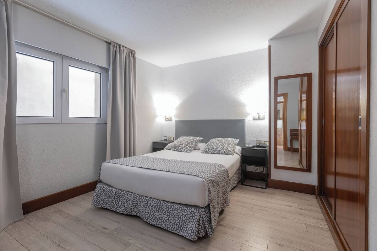 A bedroom with a bed, bedside tables, a wardrobe, and a window with curtains.