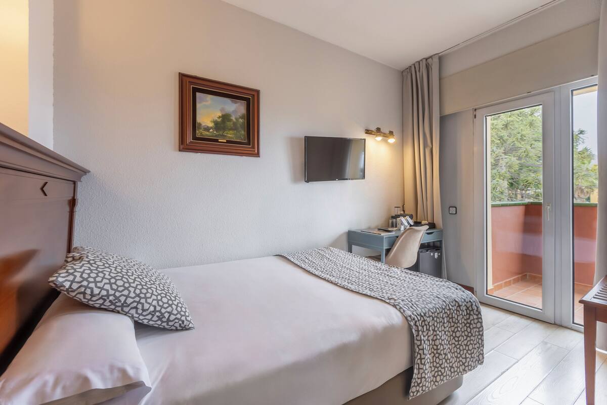 A hotel room with a bed, a desk, a chair, a TV, and a balcony with a sliding door.