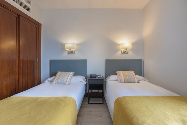A hotel room with two single beds, a wooden wardrobe, a small bedside table with a lamp, and a nightstand with a phone and charger. - Hotel Soho Boutique Los Naranjos (Málaga)