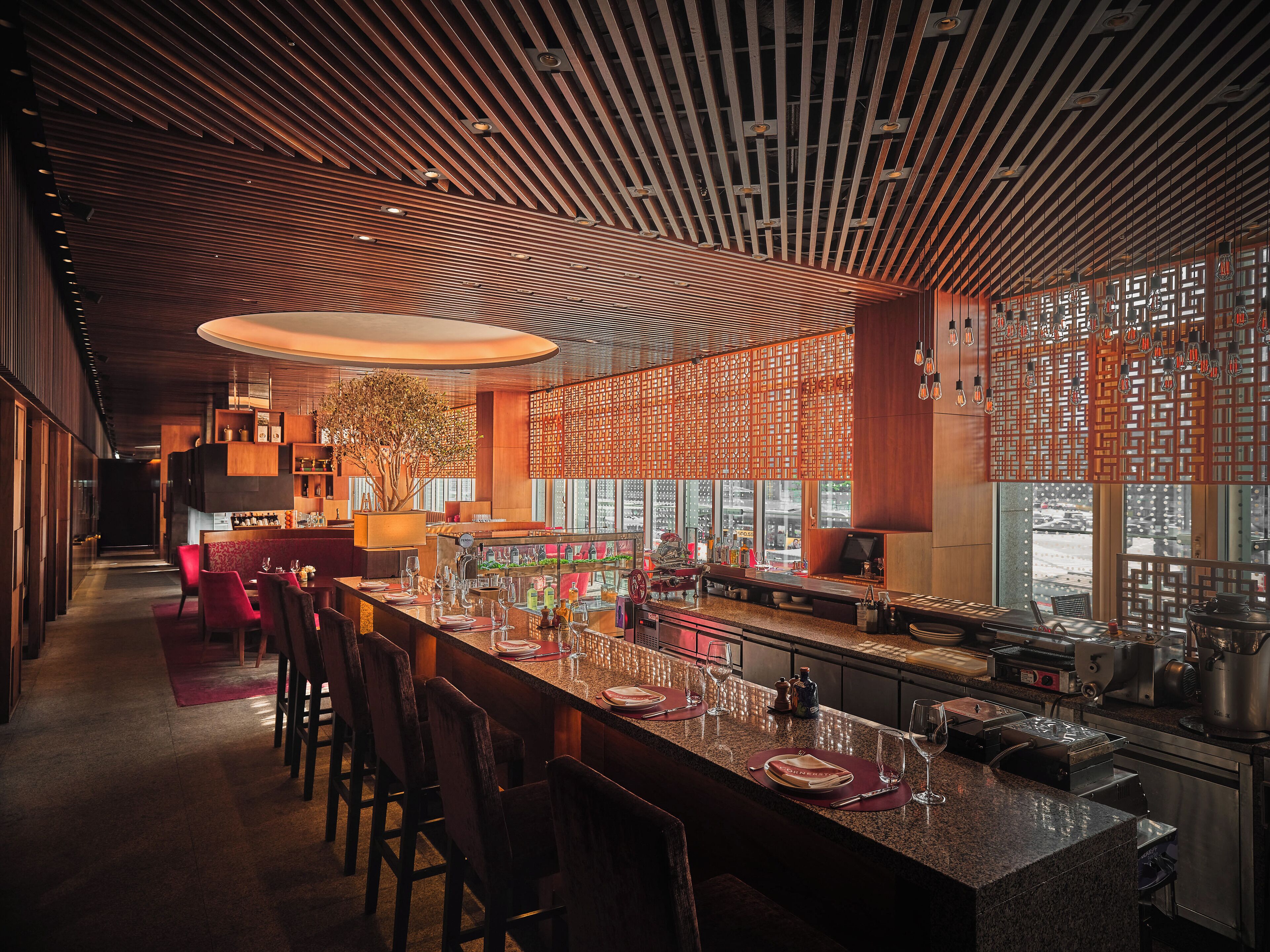 A modern bar area with a long counter, bar stools, and a large potted plant.