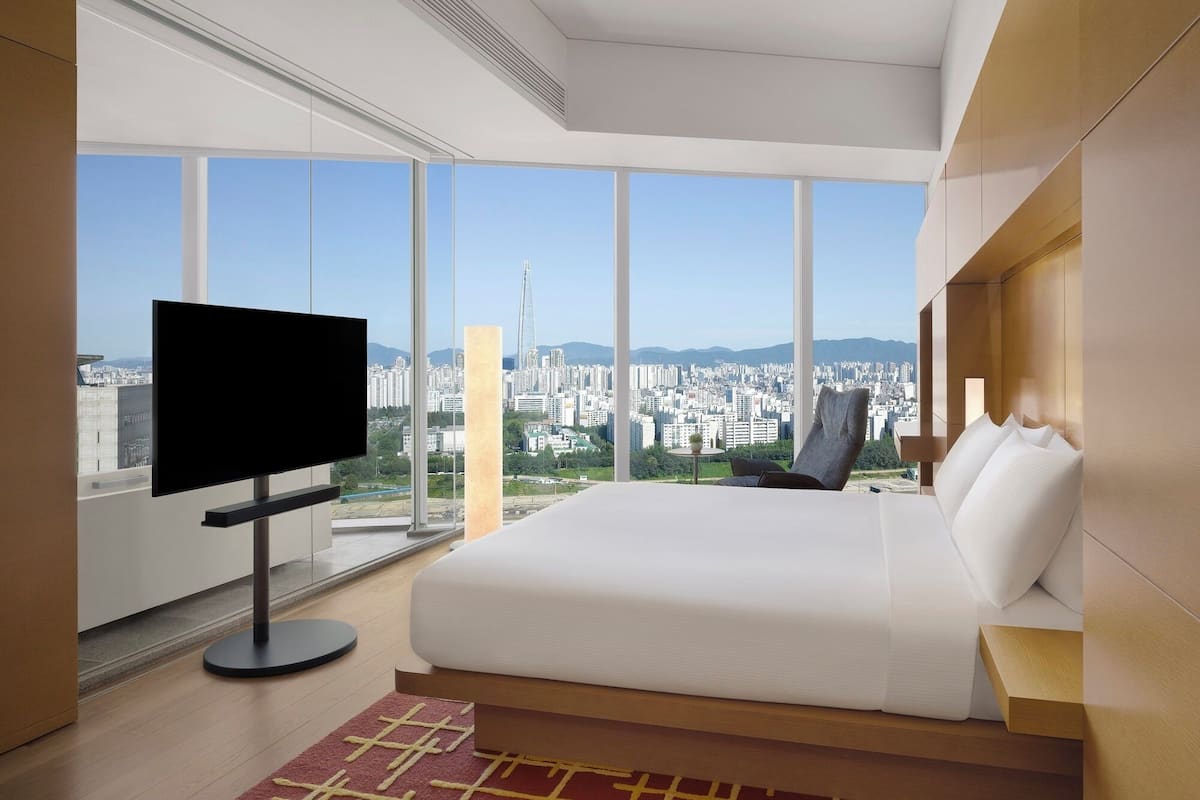 Quarto de hotel moderno com uma cama grande, televisão de tela plana e vista para a cidade.