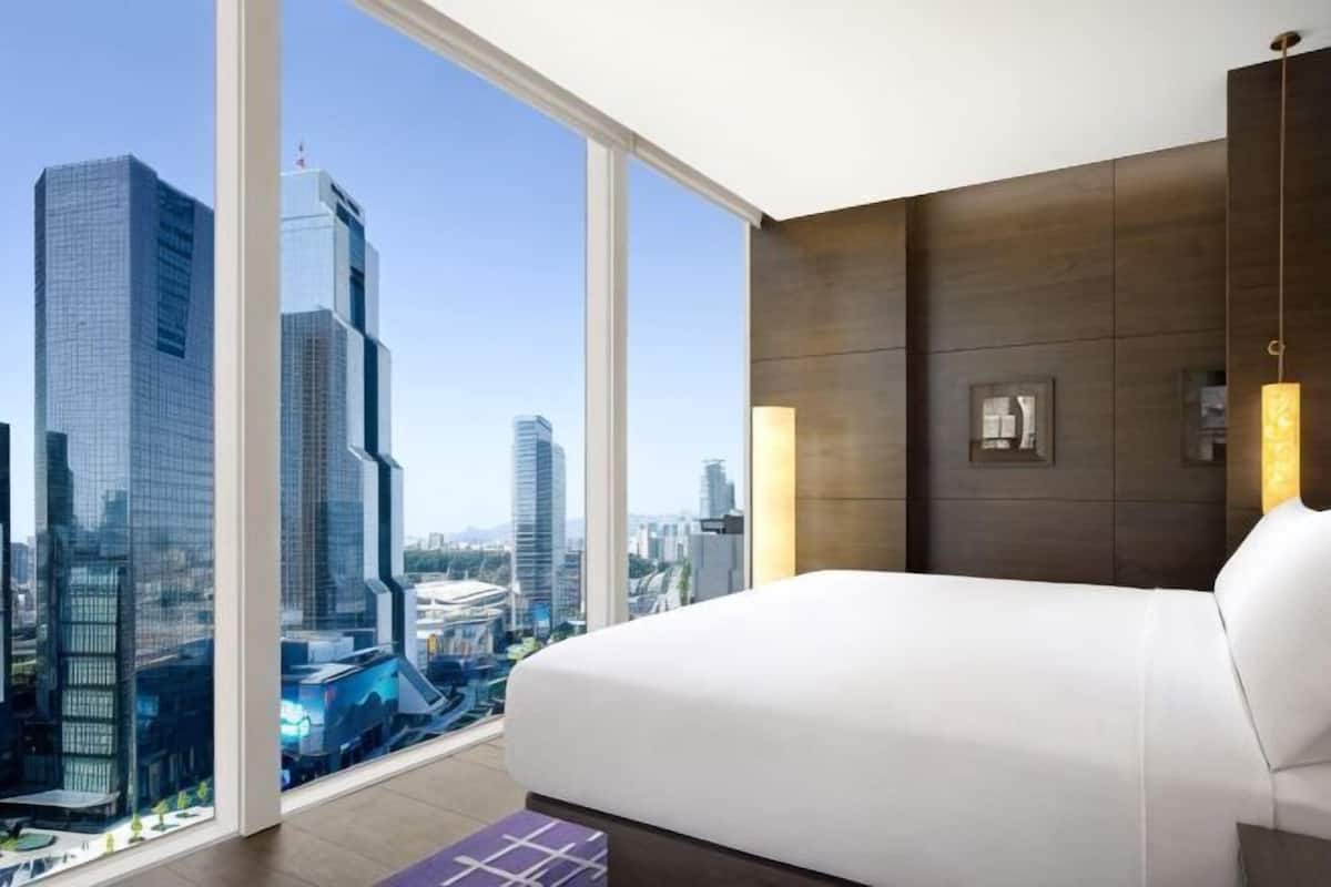 Quarto de hotel moderno com uma cama grande, vista para a cidade e uma parede de destaque em madeira.