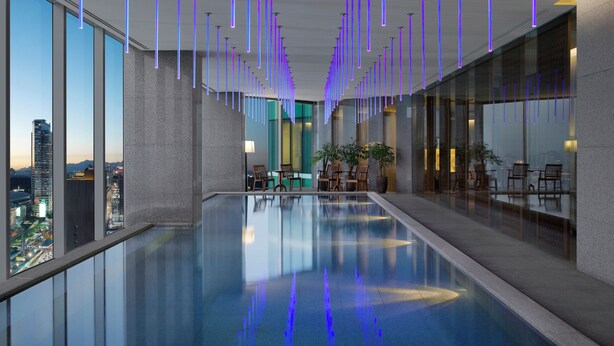 A modern indoor pool with reflective water, surrounded by glass walls and wooden chairs. - Park Hyatt Seoul (Seoul)
