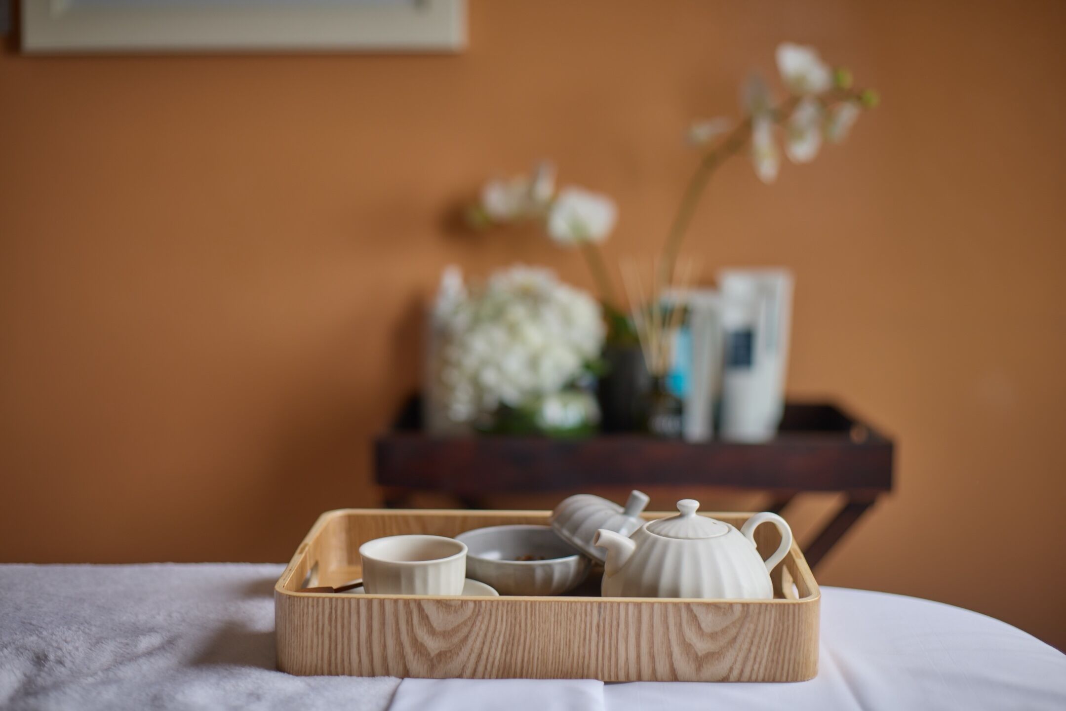Una bandeja de madera con una tetera, taza y platillo sobre una cama.