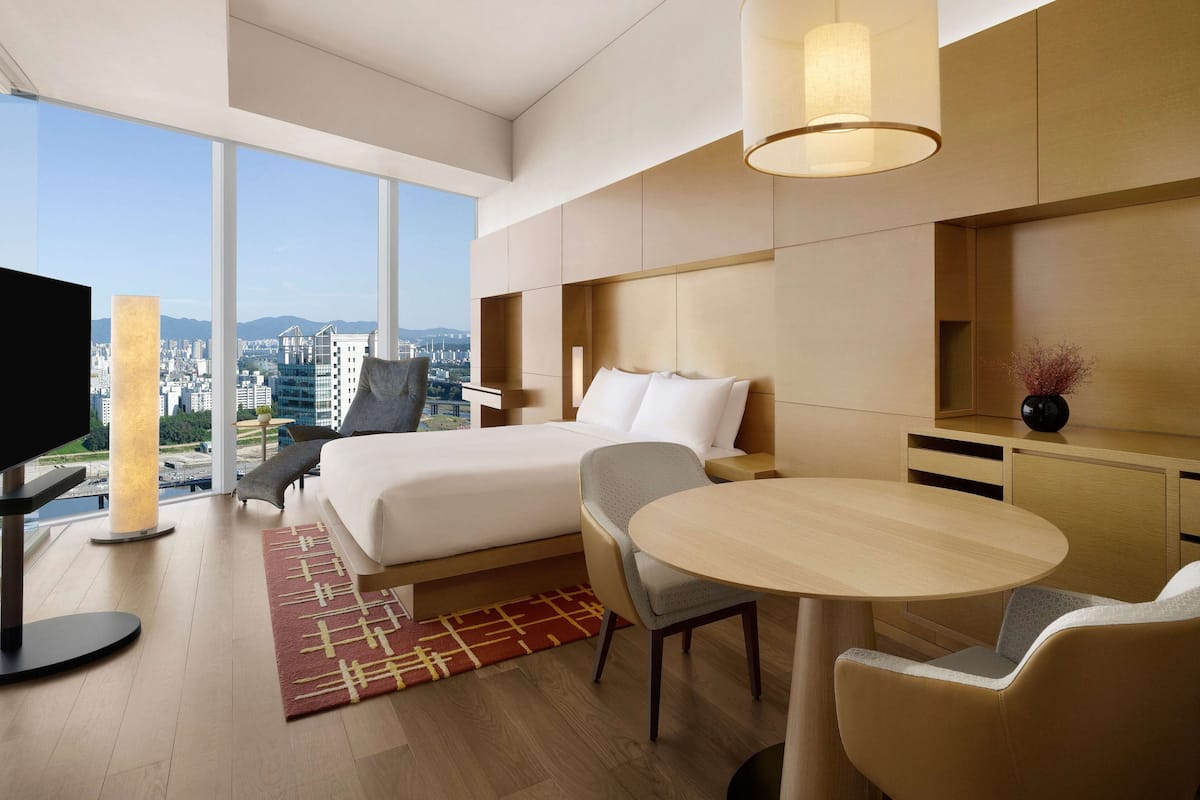Quarto de hotel moderno com uma cama grande, uma escrivaninha, uma cadeira e uma televisão.