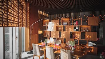 A modern dining area with a wooden table and chairs, a floor lamp, and a wall with built-in shelves displaying various items.