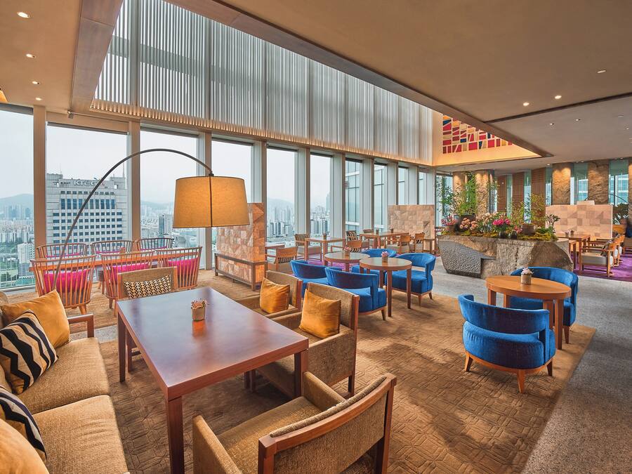 A spacious lounge area with high ceilings, large windows offering city views, and a variety of seating options including sofas and chairs.