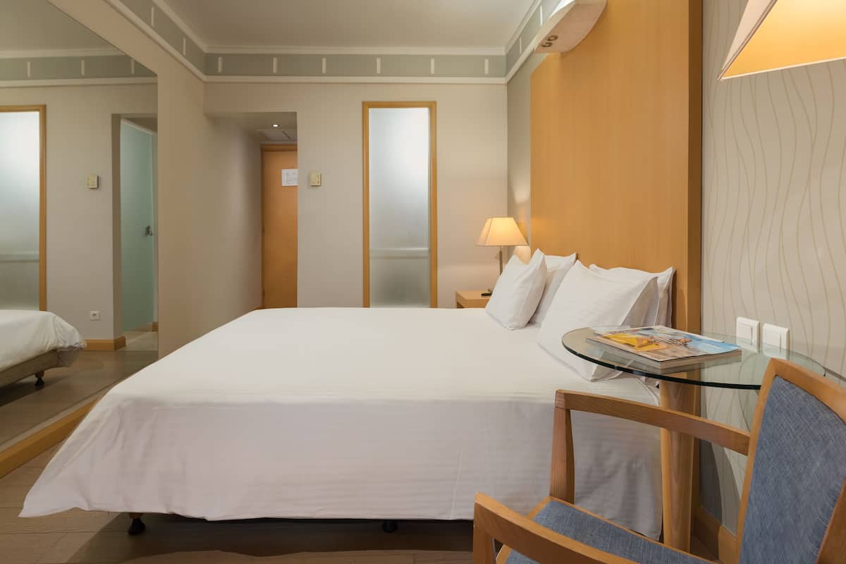 Habitación de hotel con una cama grande, una mesa de vidrio, una silla y una mesita de noche con lámpara.