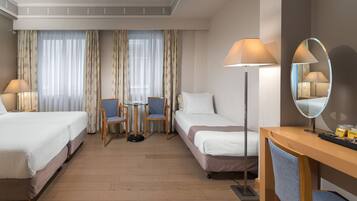 A hotel room with two beds, a desk, a chair, a table, and a floor lamp.