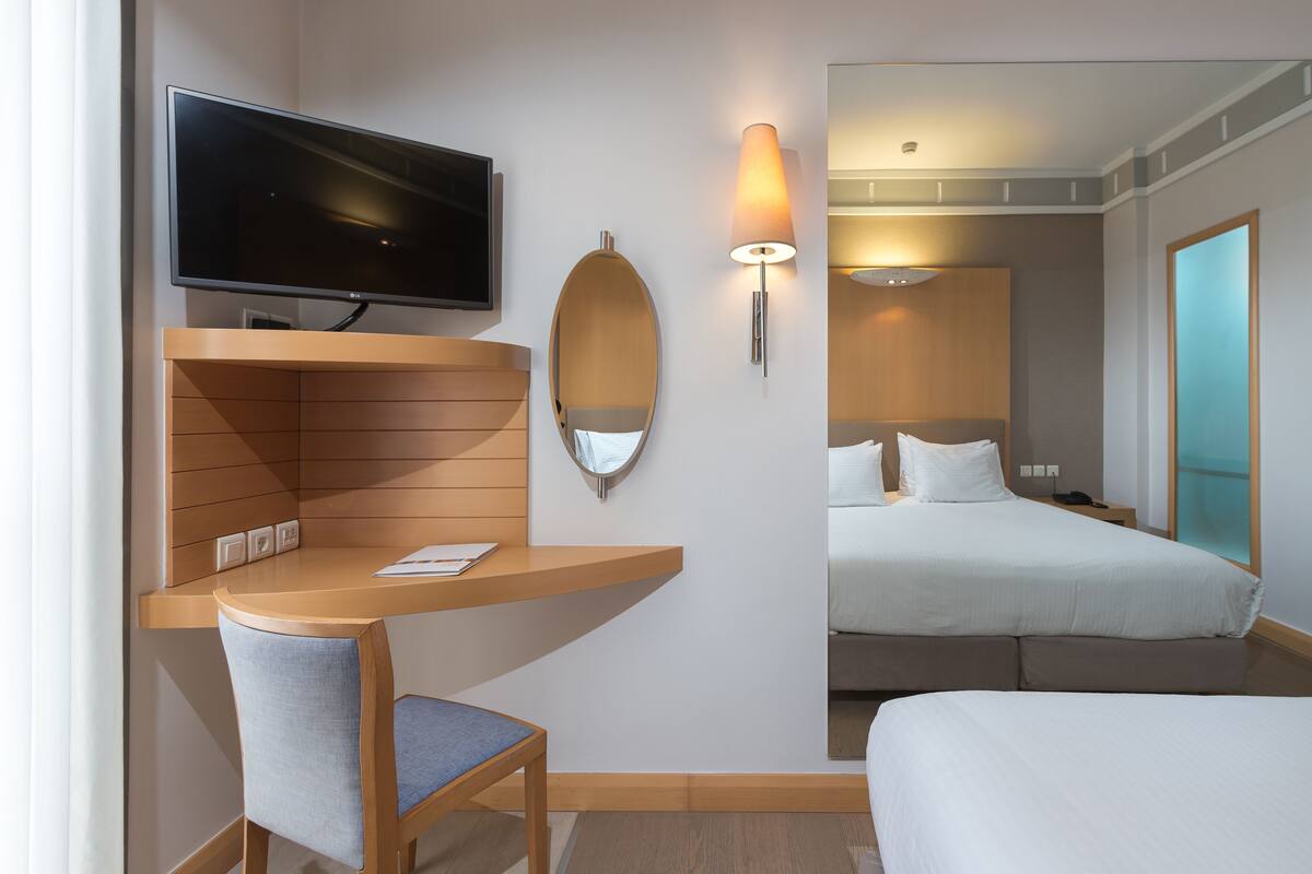 Habitación de hotel con televisión, escritorio con silla, cama y lámpara de pared.