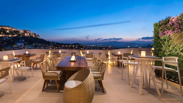 A rooftop terrace with tables and chairs, overlooking a cityscape at dusk. - Central Athens Hotel (Athens)