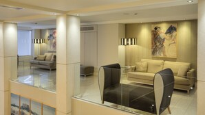 A modern hotel lobby with a glass railing, a sofa, a chair, and a painting on the wall. - Central Athens Hotel (Athens)