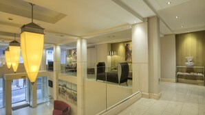 A modern hotel lobby with a glass partition, comfortable seating, and contemporary lighting fixtures. - Central Athens Hotel (Athens)
