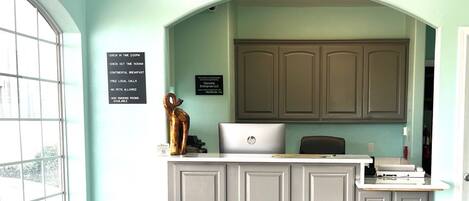 Un comptoir d’accueil avec un ordinateur portable, une sculpture en bronze et un panneau indiquant les services offerts, tels qu’un petit-déjeuner continental et les appels locaux gratuits.
