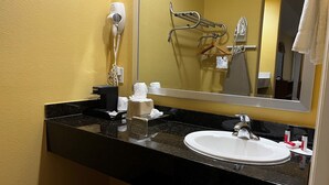 A hotel bathroom with a black granite countertop, a white sink, a hairdryer, and a mirror reflecting the bathroom. - Quality Inn Montgomery - Lake Conroe (Montgomery)