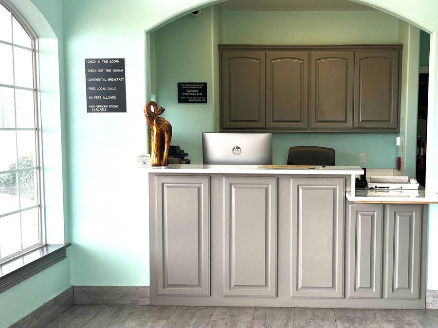 Een receptiebalie met een laptop, een bordje met faciliteiten zoals een continentaal ontbijt en rookvrije kamers, en een uitzicht door een groot raam.