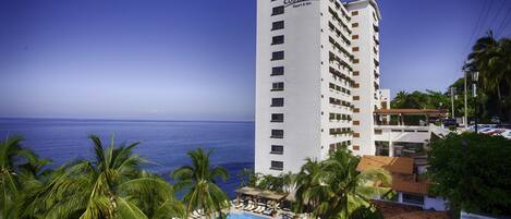 Um hotel moderno com piscina, cercado por palmeiras e vista para o oceano.