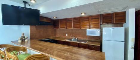 A kitchen with wooden cabinets, a built-in microwave, a refrigerator, a gas stove, and a bar area with chairs.
