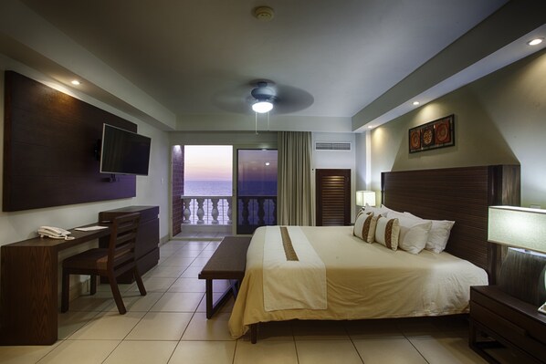 A hotel room with a bed, desk, chair, TV, and a balcony with a view. - Costa Sur All Inclusive Resort (Puerto Vallarta)