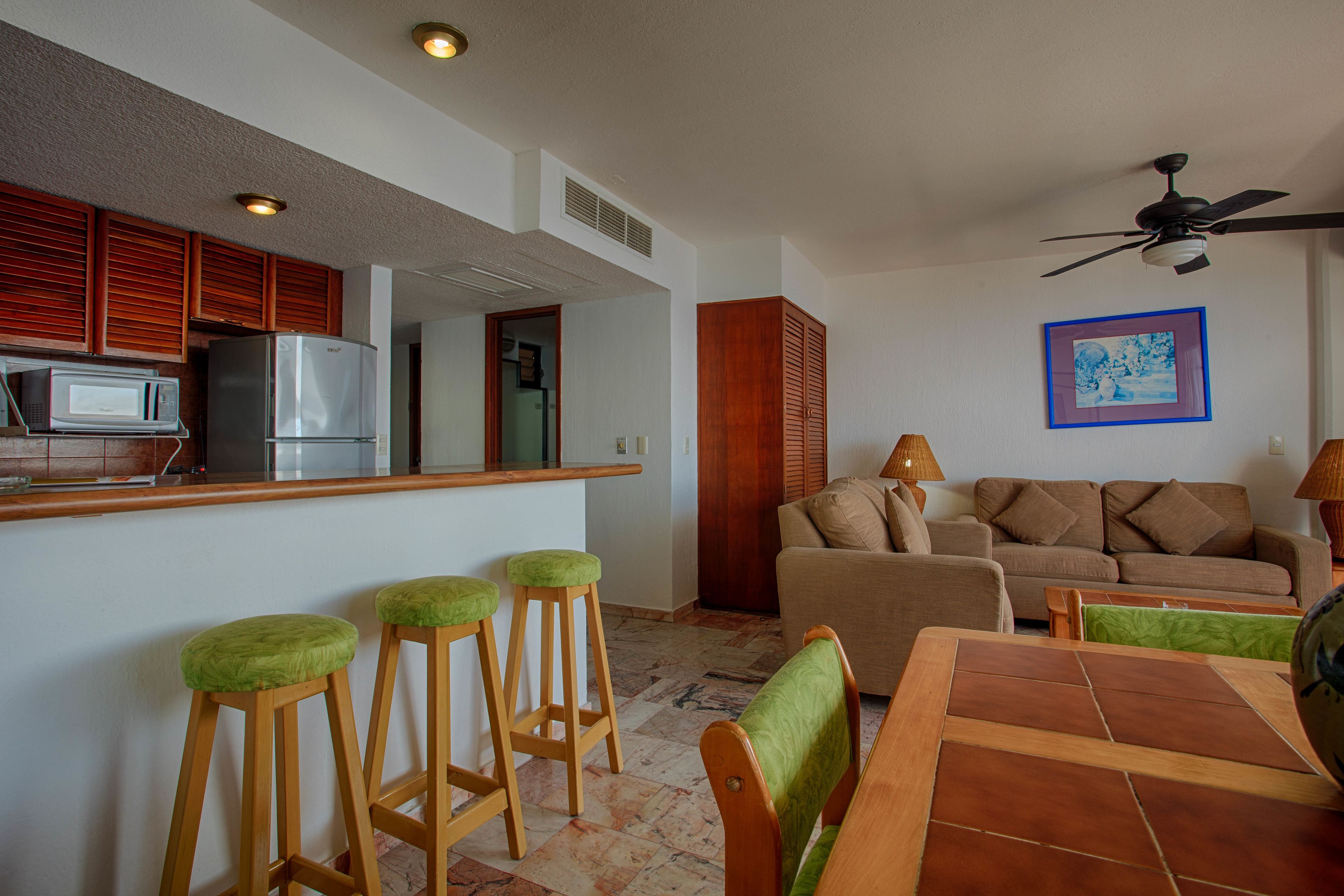 A kitchen with a microwave and refrigerator, a dining area with a table and chairs, and a living room with a sofa and lamps.