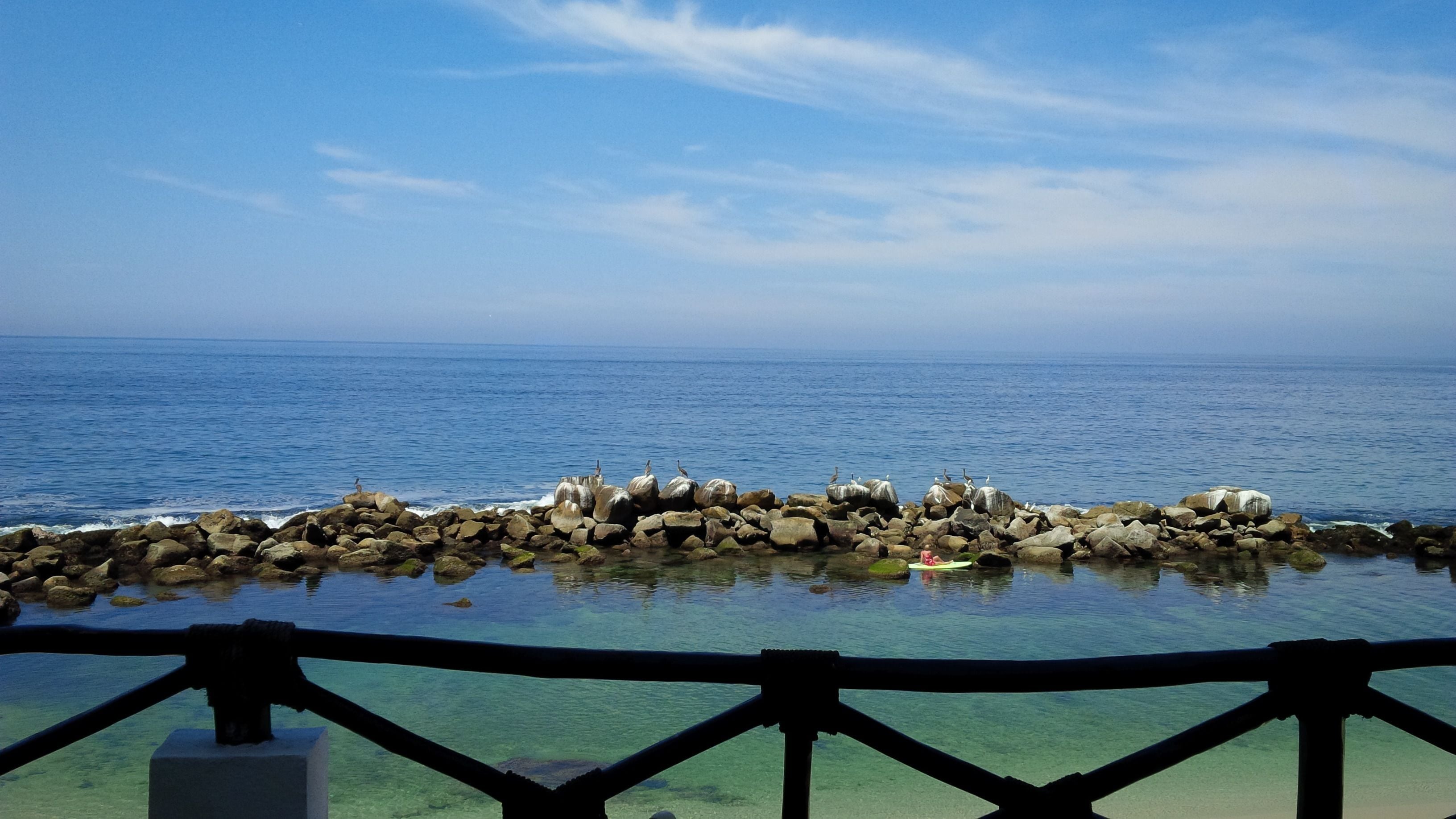 Vista despejada del océano desde un muelle rocoso con barandilla.
