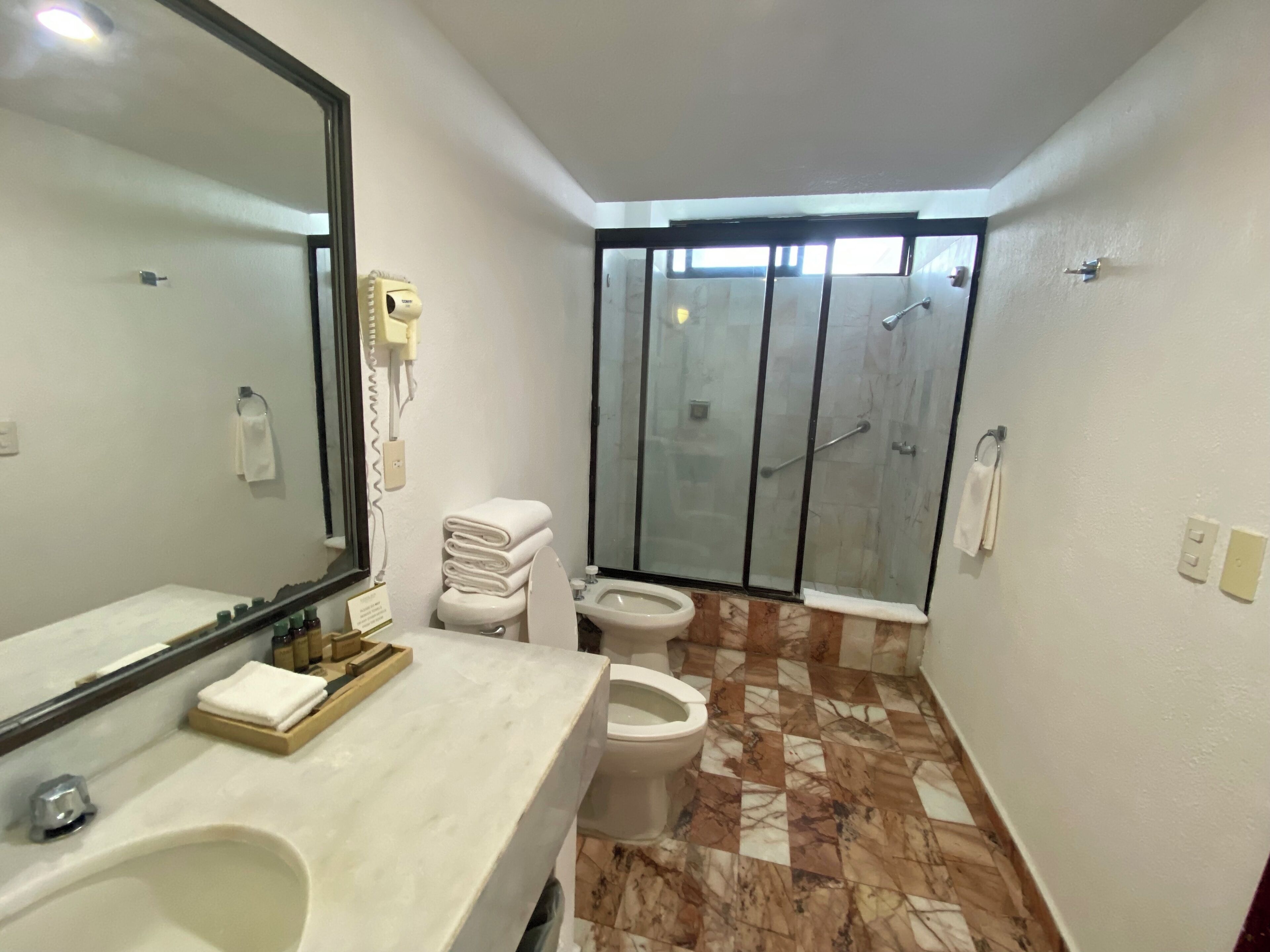 A bathroom with a large mirror, a sink, a toilet, and a shower area.