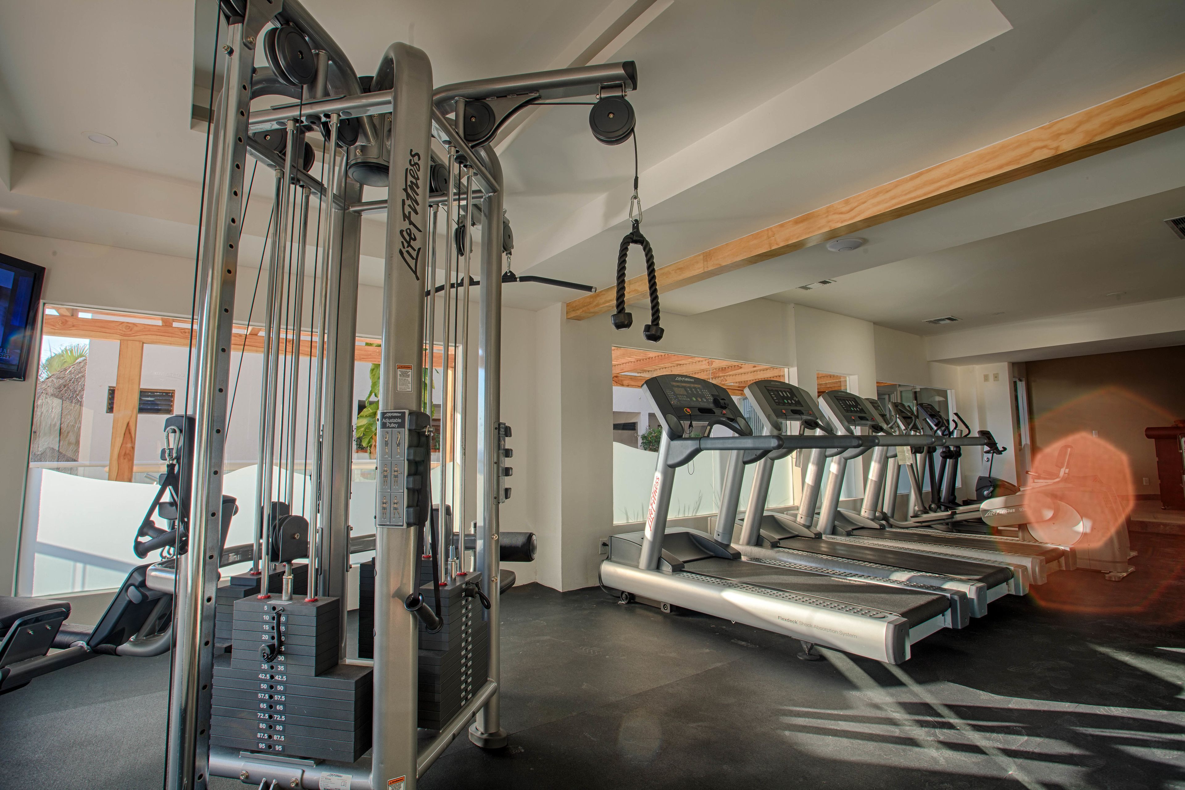 Une salle de sport équipée de tapis de course, d’une machine de musculation et d’un téléviseur fixé au mur.