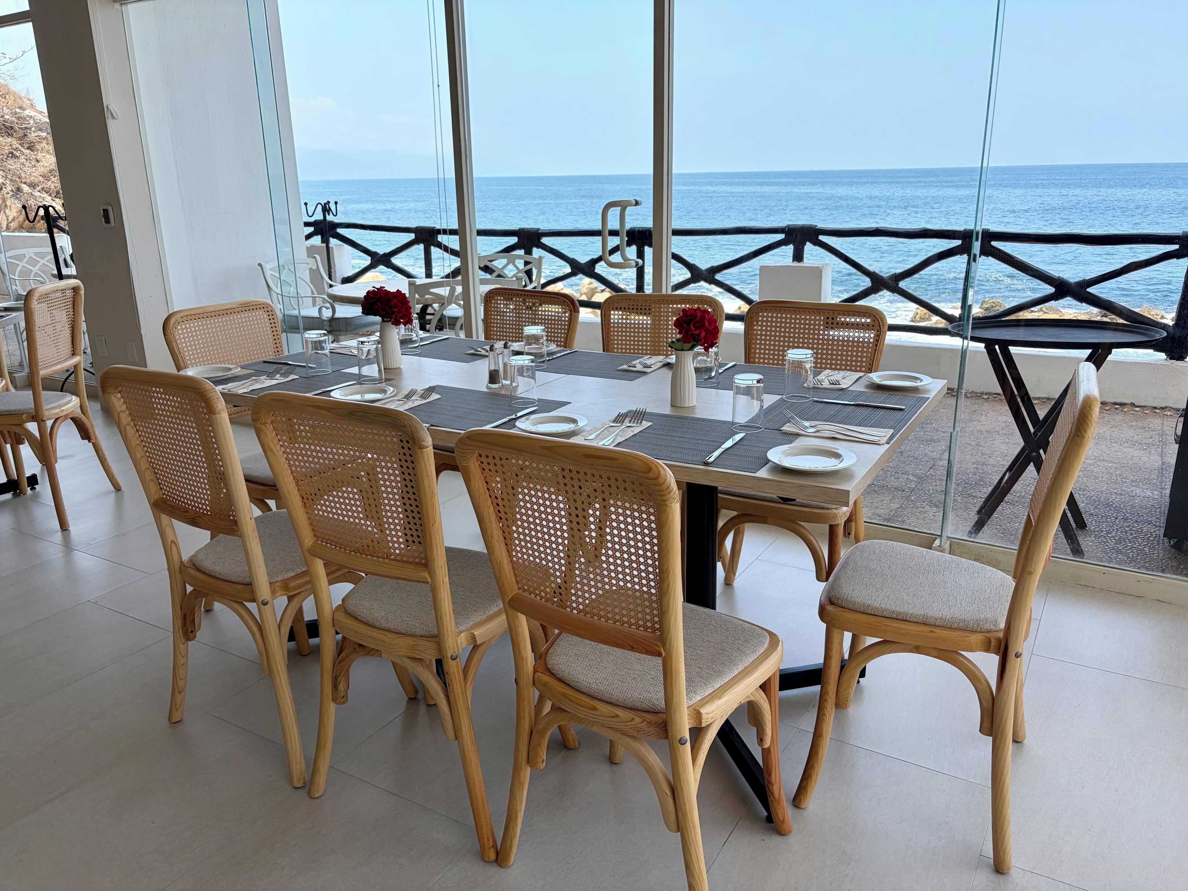 Ein Essbereich mit einem Tisch für sechs Personen, umgeben von Korbstühlen und Blick aufs Meer.