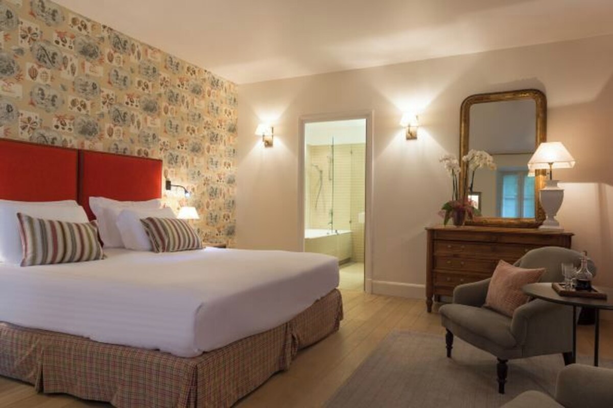 Une chambre d’hôtel avec un grand lit, une commode, une chaise et un miroir.