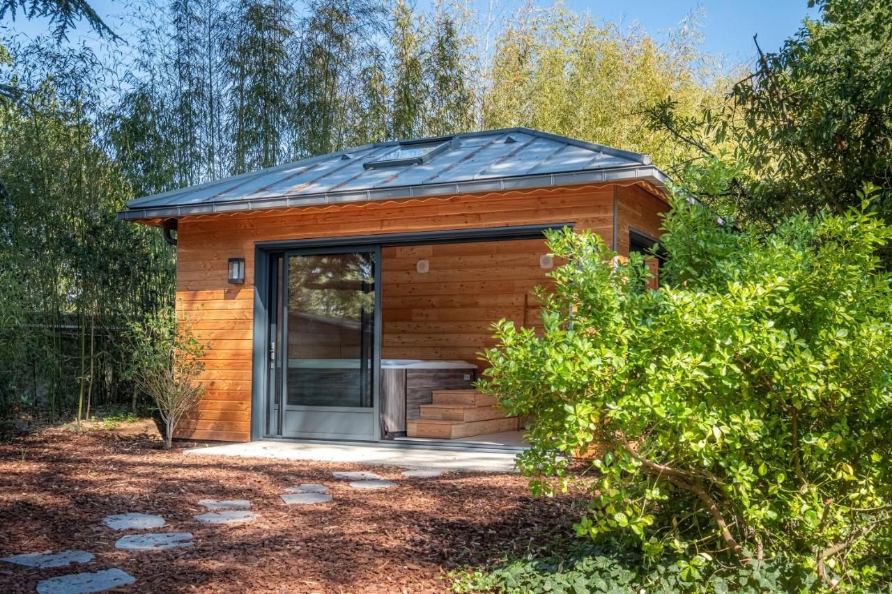 A modern wooden cabin with a glass door entrance, surrounded by a forested area.